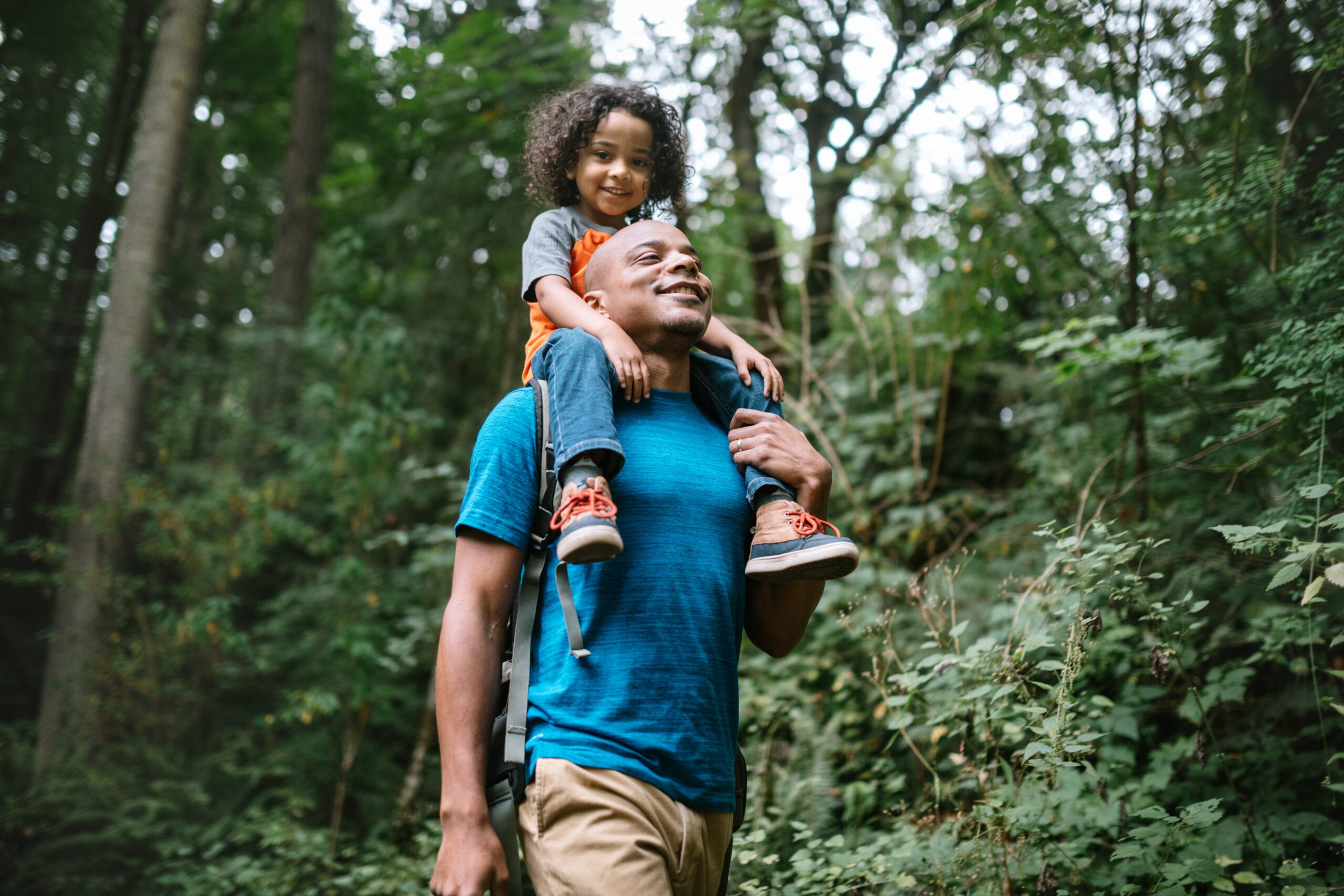 A young mixed race family spends time together outside in Washington state, enjoying the beauty of the woods in the PNW.  The dad holds his boy on his shoulders.