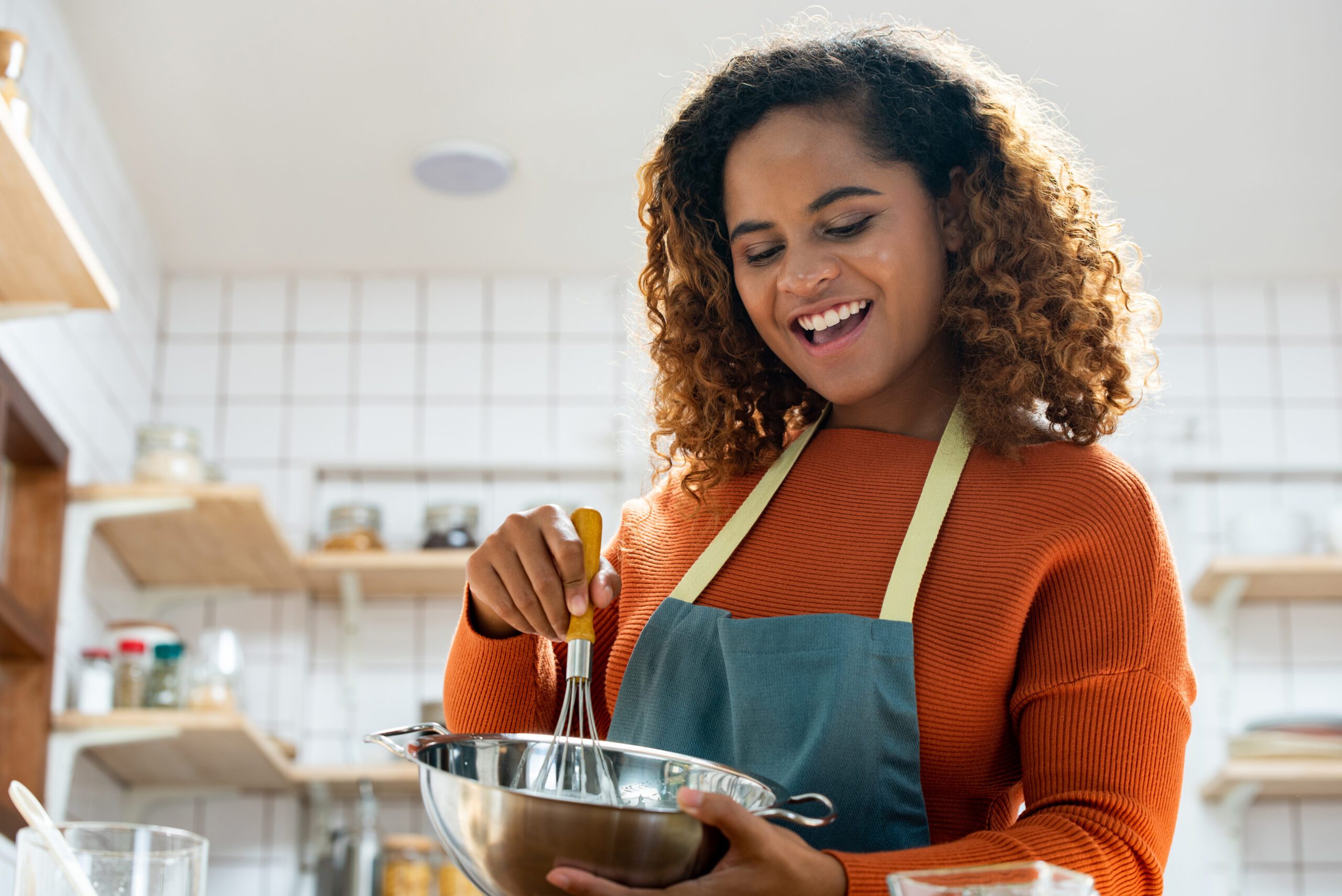 Young pretty African American woman enjoying herself cooking in kitchen while staying at home